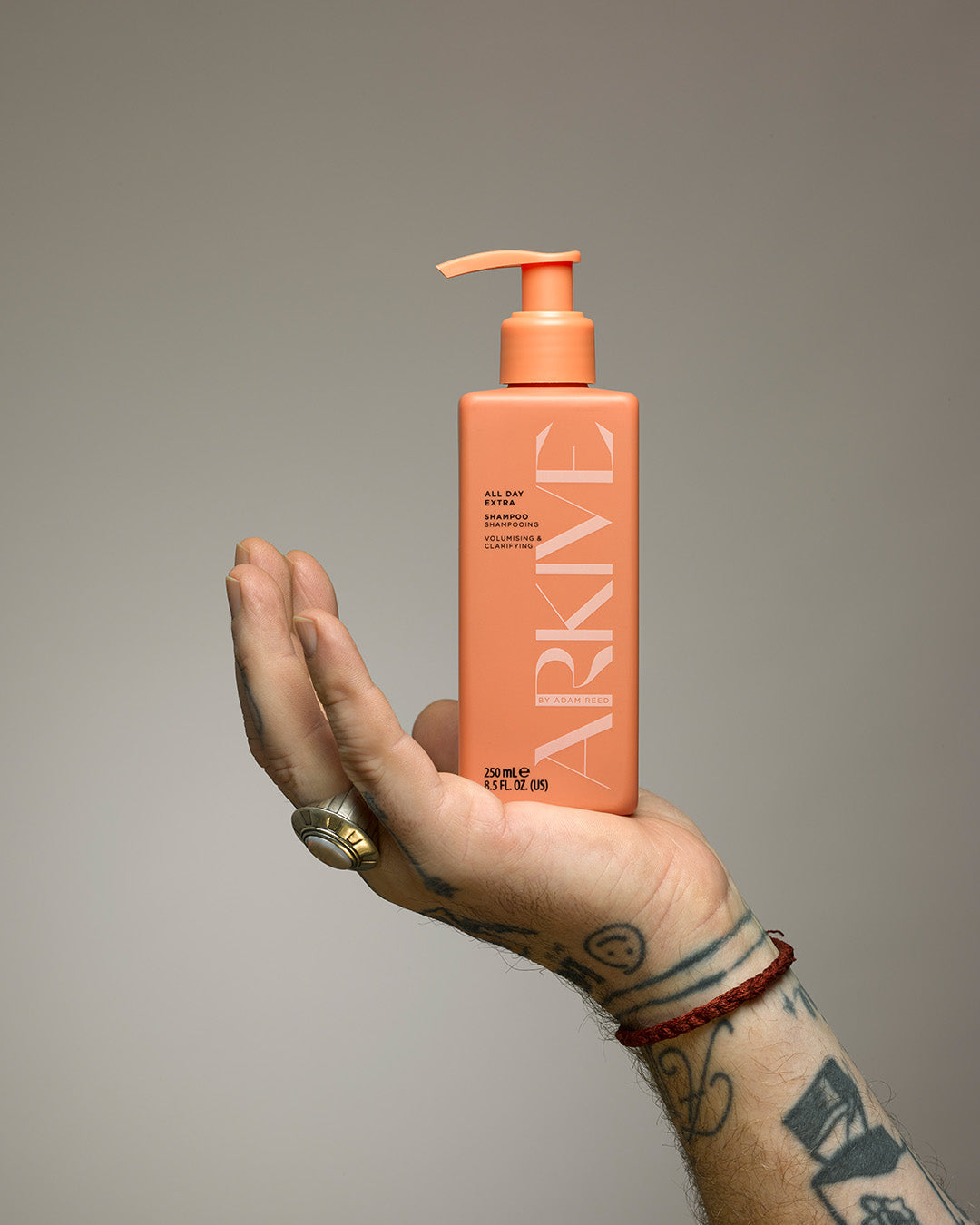 A tattooed hand holding a bottle of Arkuve's all day extra shampoo
