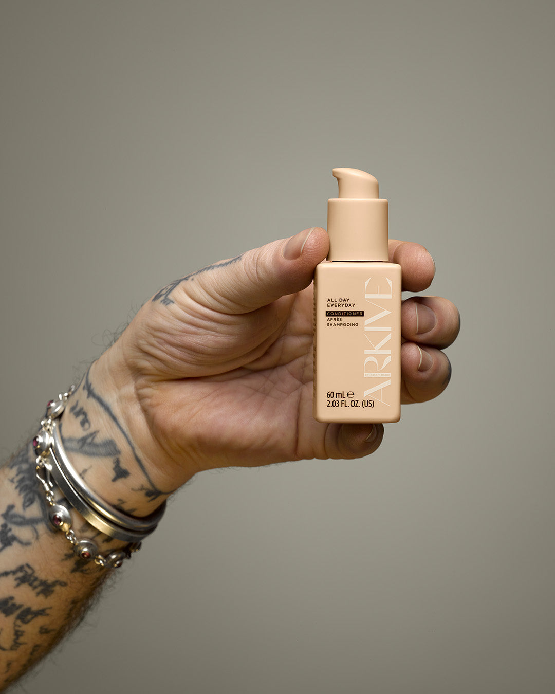 A tattooed hand holding a miniature bottle of Arkive's all day everyday conditioner