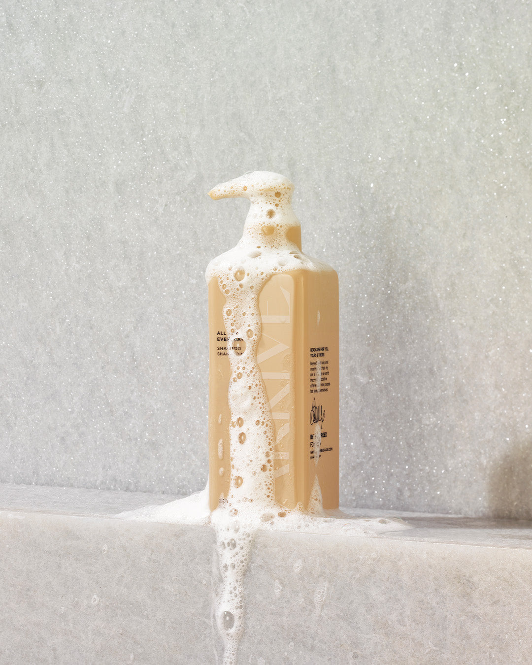 A bottle of Arkive's all day everyday shampoo resting on a shower ledge with foam