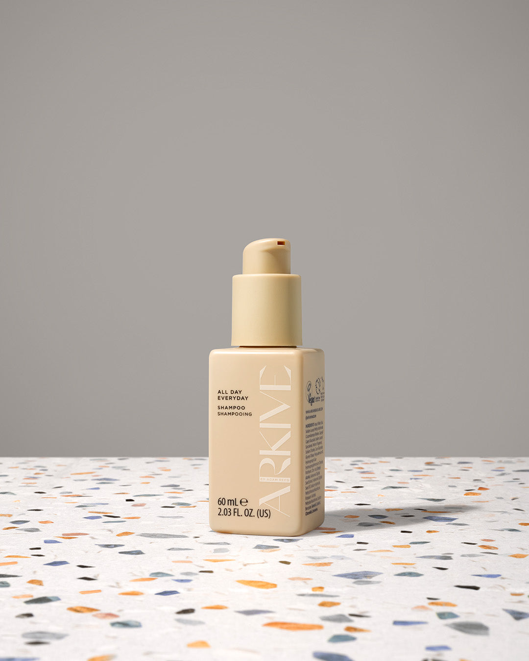 A miniature bottle of Arkive's all day everyday shampoo on a textured table