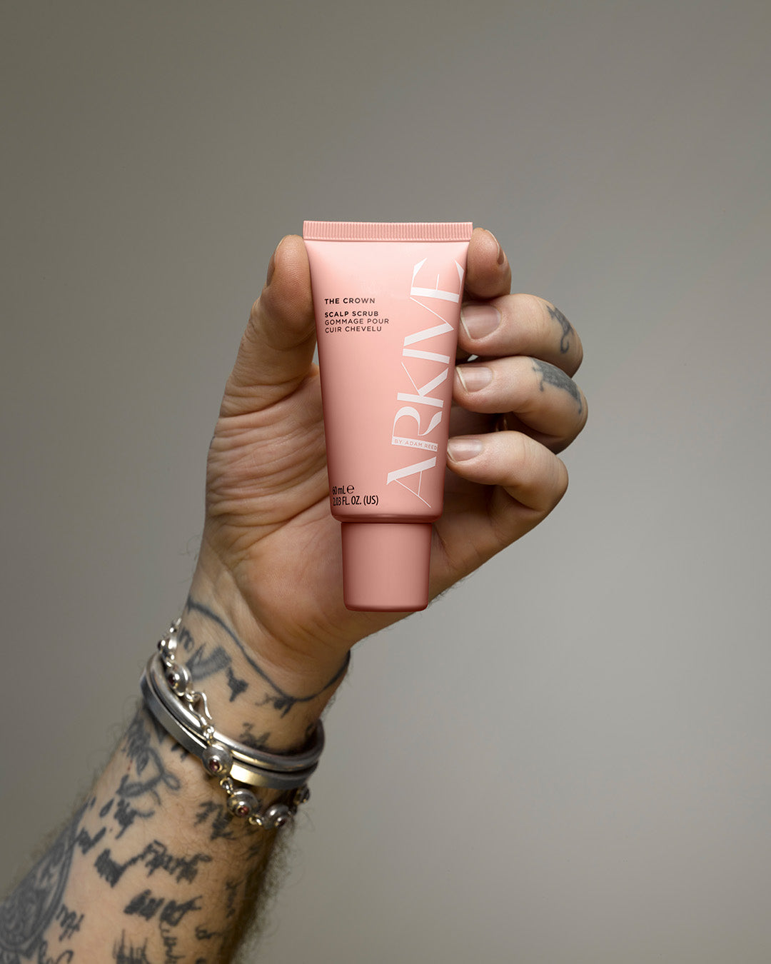 A mini bottle of Arkive's the crown scalp scrub being held in the hand